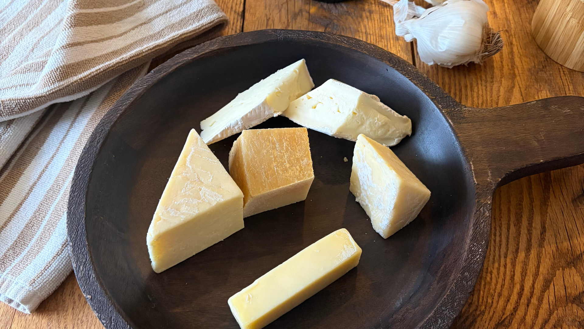 Cuts of assorted cheese on a rustic wooden plate.