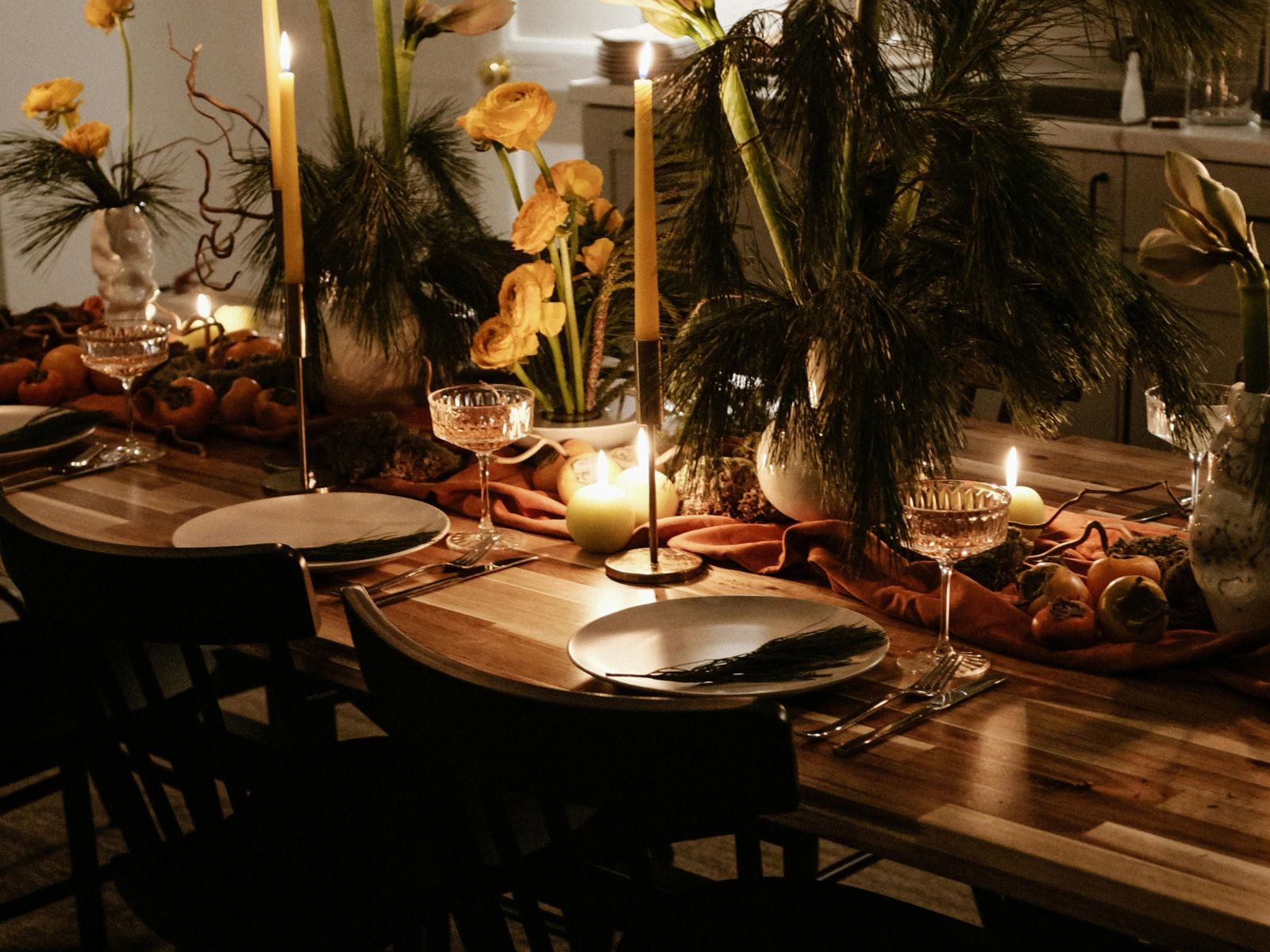 “able set with lit candles, green pine, white flowers, white plates, and wine glasses.