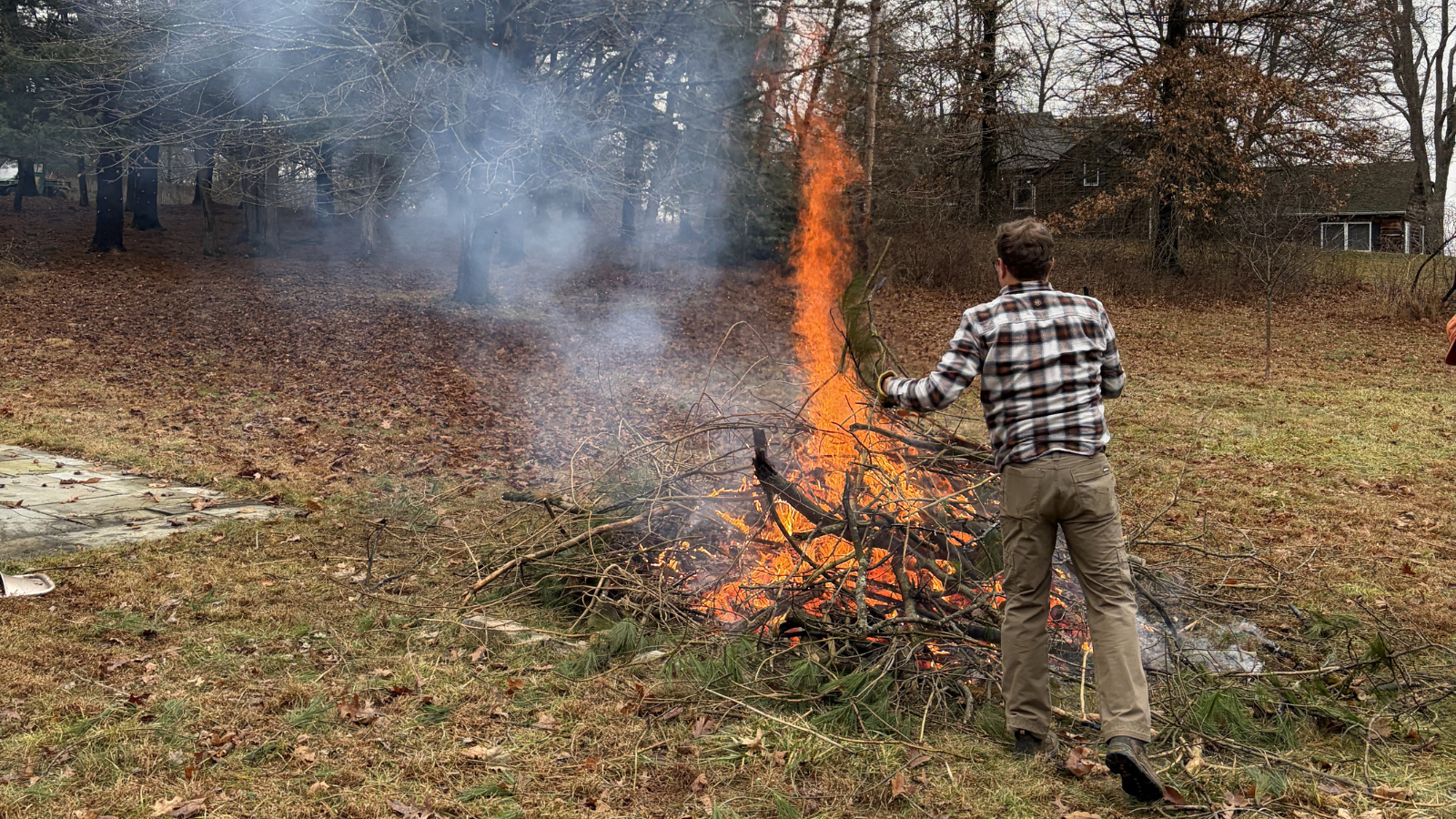 Man throwing branches onto a large fire outdoors.