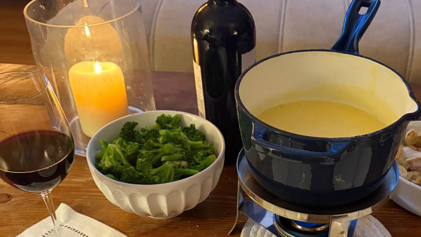 Cheese fondue for two with bread and wine on a table near a fireplace.
